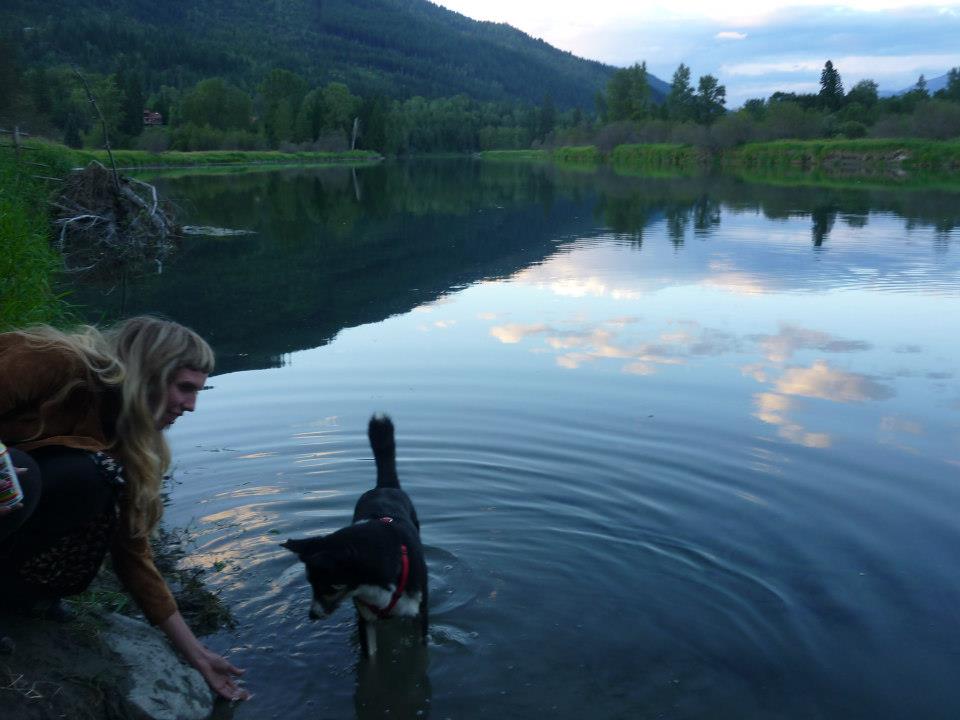 J.M. standing by a glassy lake with a dog standing in the water