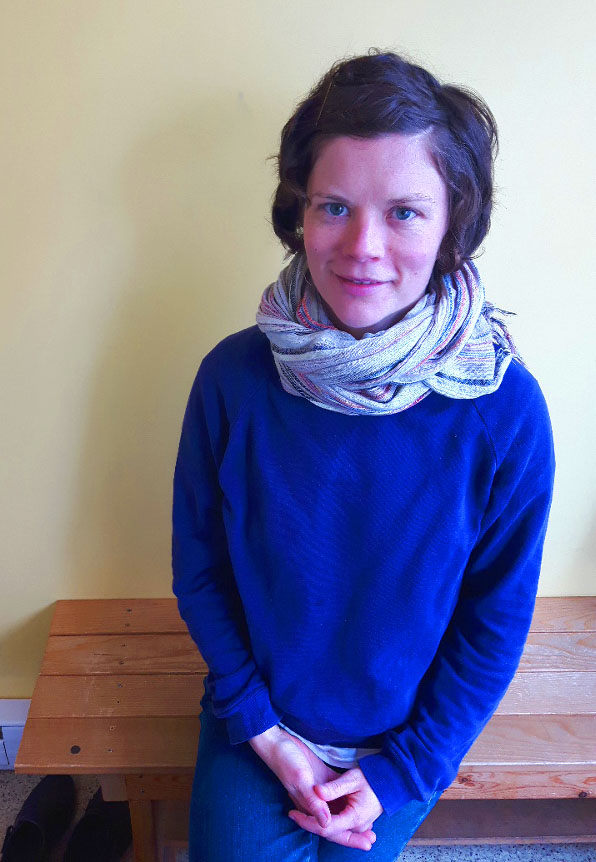 S.S. wearing a light coloured scarf and an indigo sweater sitting on the bench at Heart & Hands.