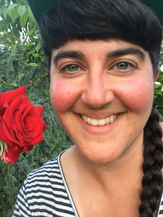 Aviva is next to a red rose, wearing a black baseball cap